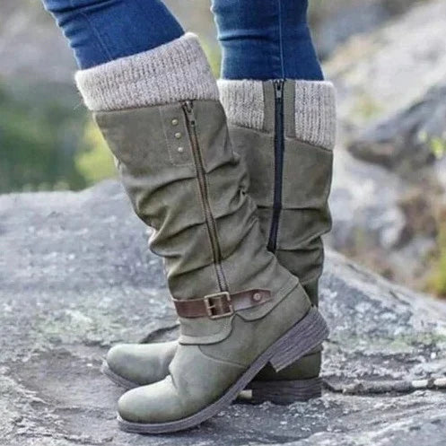 Eine Nahaufnahme eines grünen orthopädischen Stiefels mit lässigem Design und Strickbund, der von einer Person getragen wird, die auf felsigem Boden steht. Das Bild hebt sein stilvolles Aussehen und seine Komfortmerkmale hervor.