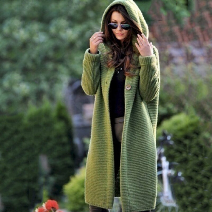 Eine Frau trägt eine lange grüne Strickjacke mit Kapuze auf weißem Hintergrund